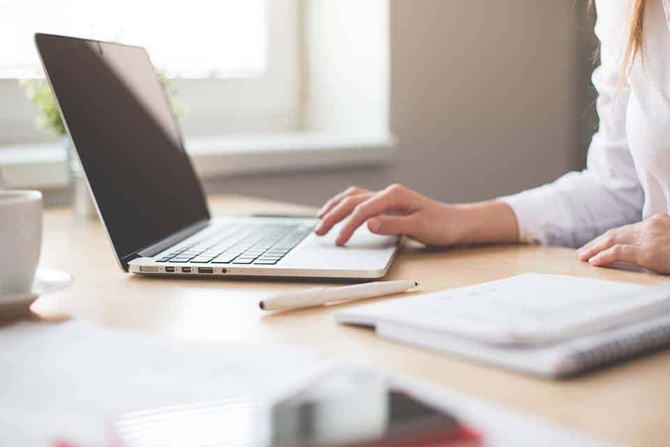 Worker sitting in front of a laptop, a notebook, and a pen
