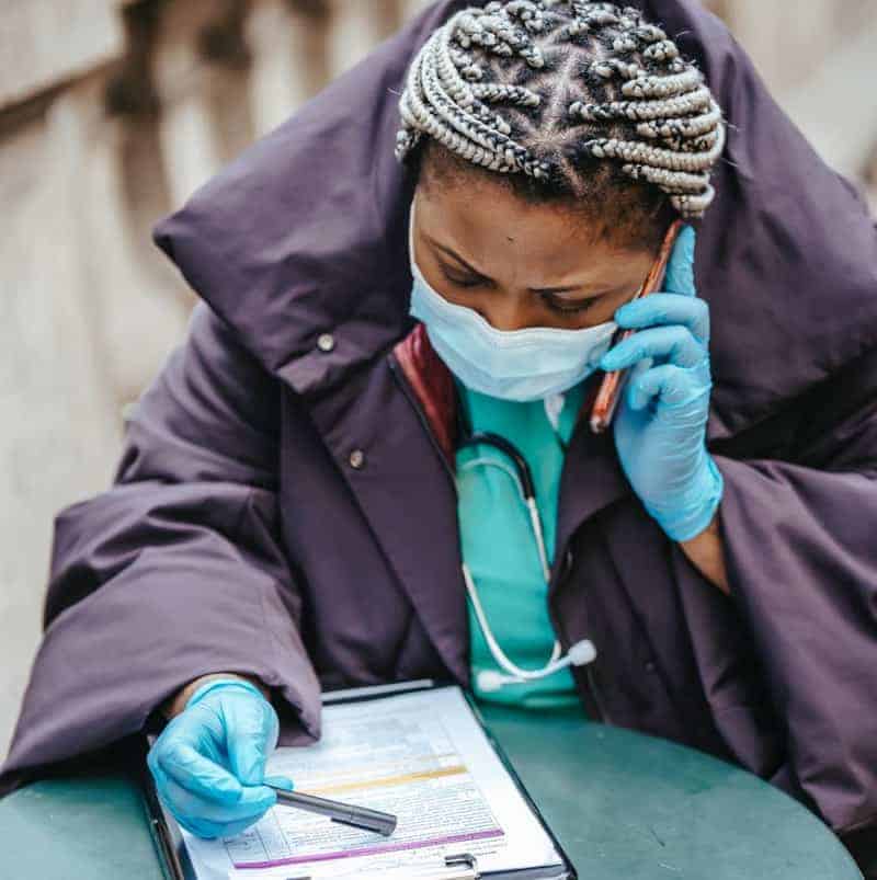 Female Black doctor with a clipboard takes a phone call