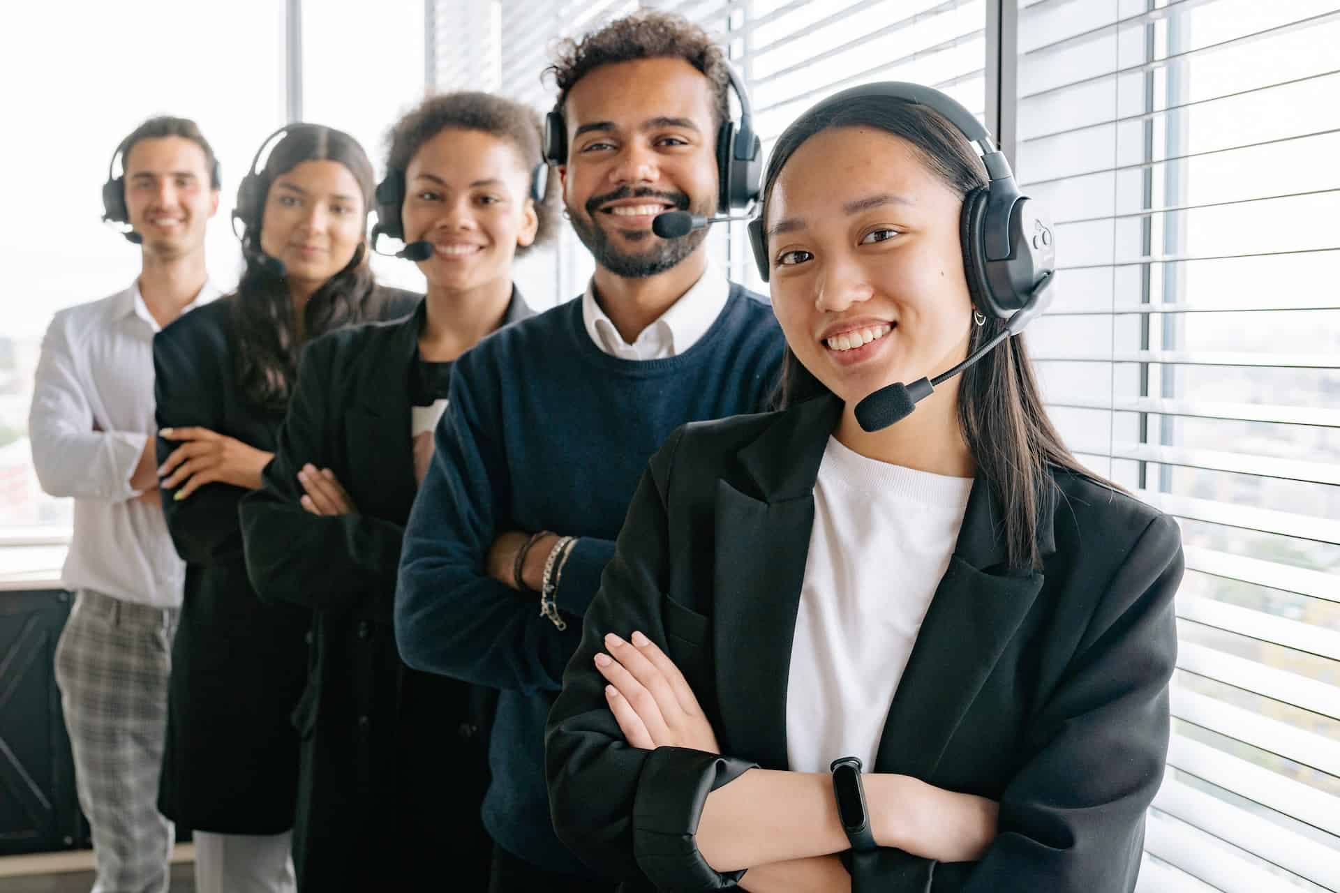 5 Call center reps smiling at camera with headsets on